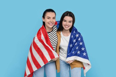 4 Temmuz - ABD 'nin Bağımsızlık Günü. Açık mavi arka planda Amerikan bayrağı taşıyan mutlu kadın ve kızı