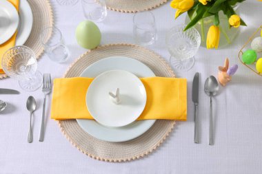 Festive table setting with glasses, painted eggs and vase of tulips. Easter celebration