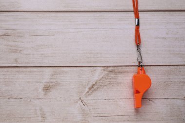 Açık ahşap masada kordonlu turuncu bir düdük, üst manzara. Metin için boşluk