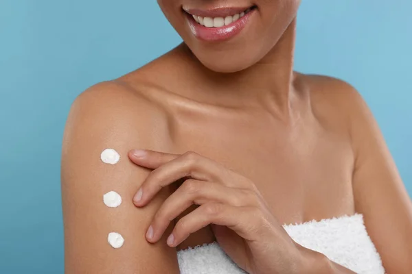 stock image Young woman applying body cream onto arm on light blue background, closeup