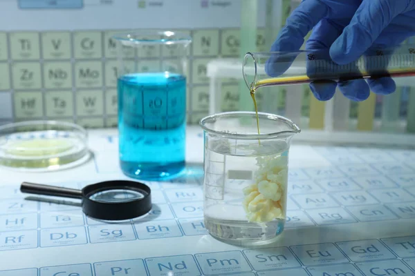 科学家将试管中的液体倒入烧杯 不同的实验室玻璃器皿和放大镜中的化学元素周期表 — 图库照片