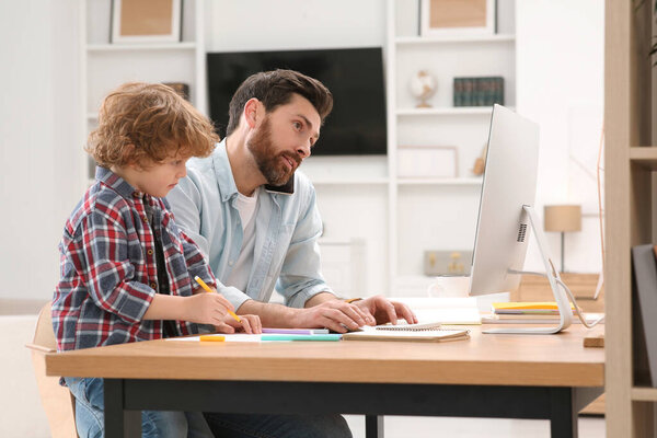 Man working remotely at home. Busy father talking on smartphone while his son drawing at desk