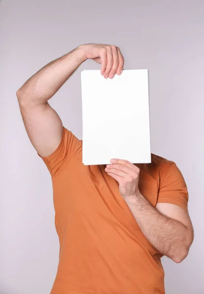 薄い灰色の背景に紙のシートで顔を覆う男 デザインのためのモックアップ — ストック写真
