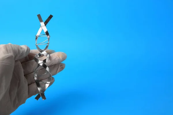 stock image Scientist with DNA molecular chain model made of metal on blue background, closeup. Space for text