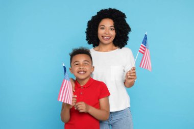 4 Temmuz - ABD 'nin Bağımsızlık Günü. Mutlu kadın ve oğlu açık mavi arka planda Amerikan bayraklarıyla