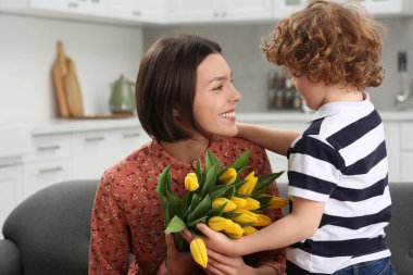 Anneler Günü 'nde annesini tebrik eden küçük bir çocuk. Sarı lale buketi tutan kadın.