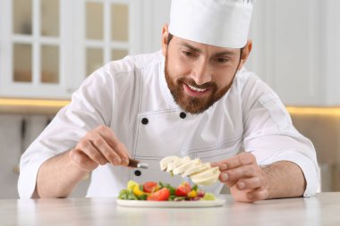 Profesyonel şef mutfaktaki mermer masada lezzetli bir salataya mozzarella ekliyor.