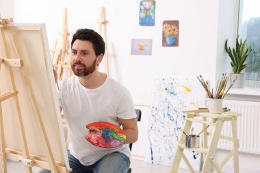 Stüdyoda resim yapan adam. Tuvali tutmak için resim sehpası kullanılıyor