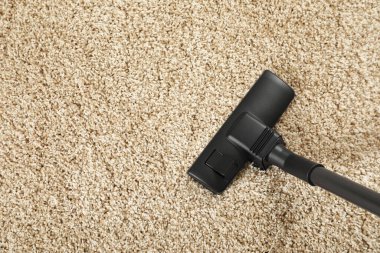 Modern elektrikli süpürgeyle bej halıları süpürüyor. Metin için boşluk