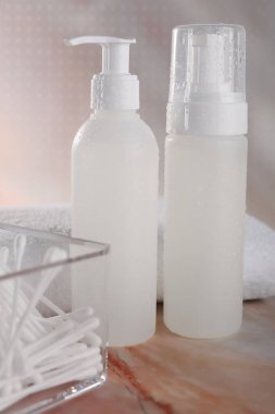 Bej mermer masa üzerinde yüz temizleme ürünleri ve pamuk tomurcukları olan şişeler.