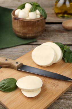 Lezzetli mozzarella dilimleri, fesleğen yaprakları ve ahşap masa üzerinde bıçak.