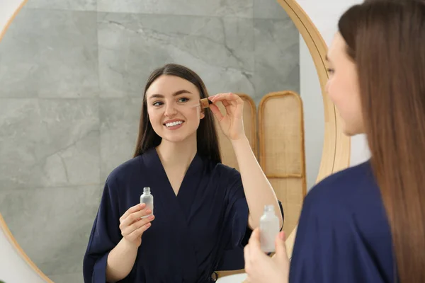 Vacker Kvinna Blå Morgonrock Applicera Ansiktsserum Nära Spegeln Inomhus — Stockfoto