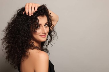 Açık gri arka planda uzun kıvırcık saçlı güzel bir genç kadın. Metin için boşluk