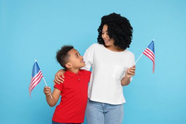 4 Temmuz - ABD 'nin Bağımsızlık Günü. Mutlu kadın ve oğlu açık mavi arka planda Amerikan bayraklarıyla