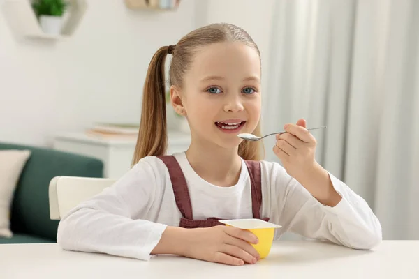 可爱的小女孩 在屋里的白桌边吃美味的酸奶 — 图库照片