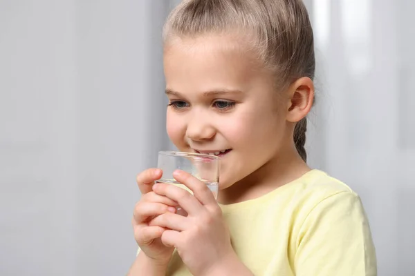 小女孩在室内用玻璃杯喝水 — 图库照片