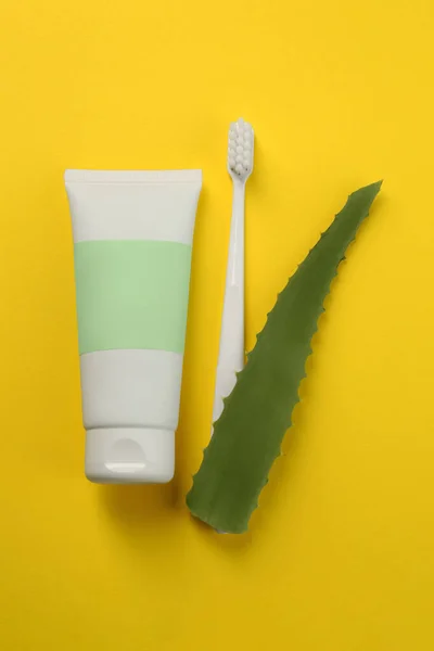 stock image Aloe vera toothpaste in blank tube, brush and green leaf on yellow background, flat lay. Space for text