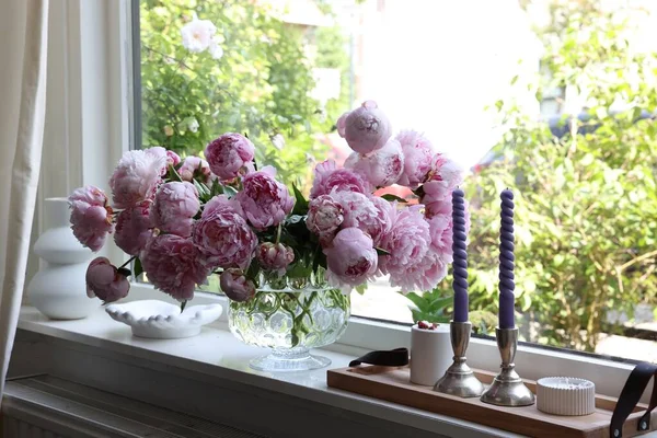 stock image Beautiful pink peonies in vase and tray with candles on window sill. Interior design