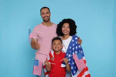 4 Temmuz - ABD 'nin Bağımsızlık Günü. Açık mavi arka planda Amerikan bayrakları olan mutlu bir aile.