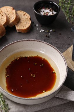 Koyu gri masada bir kase balzamik sirke, yağ, baharat ve ekmek.