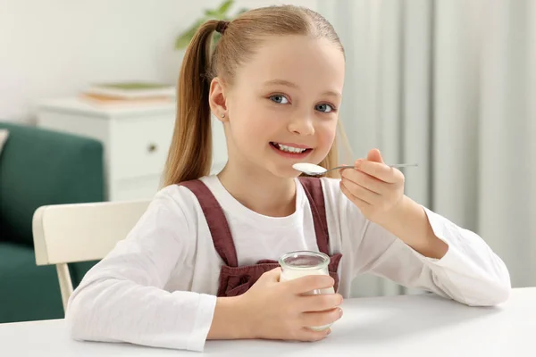 可爱的小女孩在家里的白桌边吃着美味的酸奶 — 图库照片