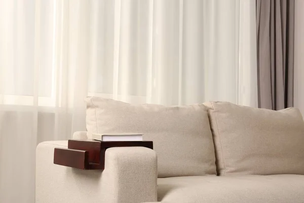 Stock image Wooden armrest table with book on sofa in room. Interior element