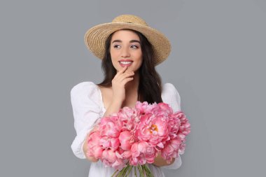 Gri arka planda pembe şakayık demeti olan hasır şapkalı güzel bir kadın.