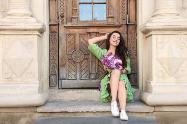 Baharda çiçek buketi olan güzel bir kadın açık hava binasının yanında, yazı yazmak için yer var.