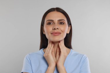 Endocrine system. Young woman doing thyroid self examination on light grey background clipart