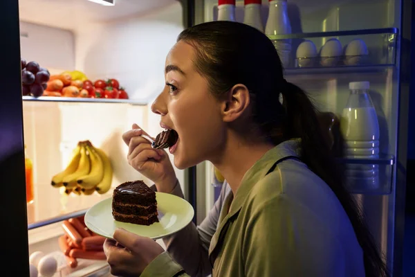 年轻女人晚上在厨房冰箱边吃蛋糕 坏习惯 — 图库照片