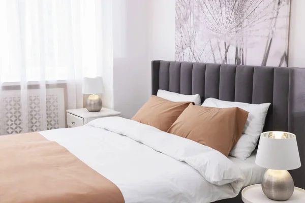 明るい部屋のベッドサイドテーブルに快適なベッドとランプ スタイリッシュなインテリア — ストック写真