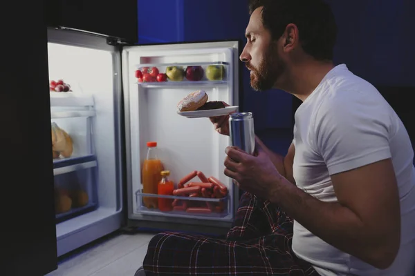 晚上拿着甜甜圈在厨房冰箱边喝酒的男人 坏习惯 — 图库照片