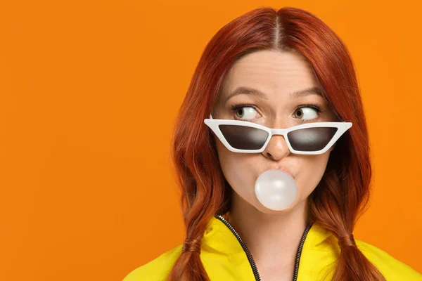 stock image Emotional woman in sunglasses blowing bubble gum on orange background. Space for text