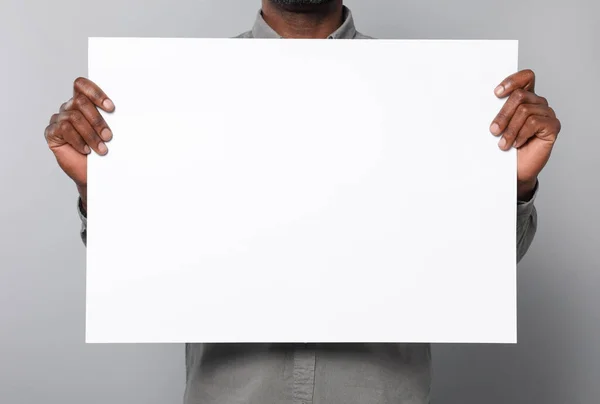 灰色の背景に紙のシートを保持アフリカ系アメリカ人男性は クローズアップ デザインのためのモックアップ — ストック写真