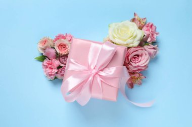 Hediye kutusu ve açık mavi arka planda güzel çiçekler, düz yatıyordu.