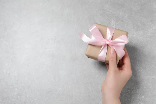 女人拿着礼品盒 粉红的蝴蝶结在浅灰色的桌子上 顶视图 案文的篇幅 — 图库照片