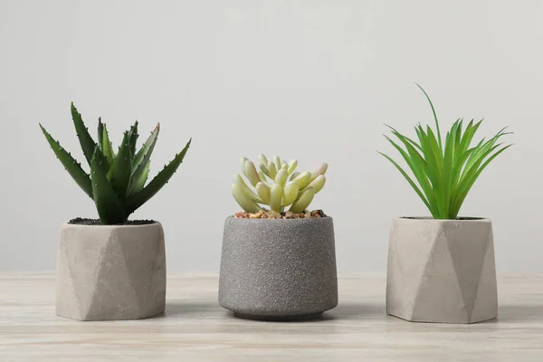 薄灰色の背景を持つ木製のテーブルの上の花の鍋に多くの異なる人工植物 — ストック写真