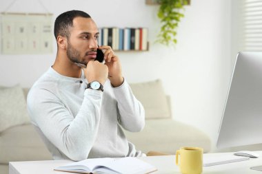 Odada bilgisayarla çalışırken akıllı telefondan konuşan genç bir adam. Merkez Ofis