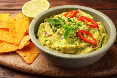 Tahta masada bir kase lezzetli guacamole, limon ve tortilla cipsi, yakın plan.