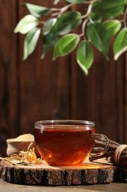 Bardakta Aromatik meyan kökü çayı ve tahta masada kurutulmuş meyan kökü çubukları, metin için yer.