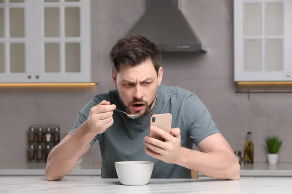 台所のテーブルで朝食をとりながらスマホを使う男 インターネット中毒 — ストック写真
