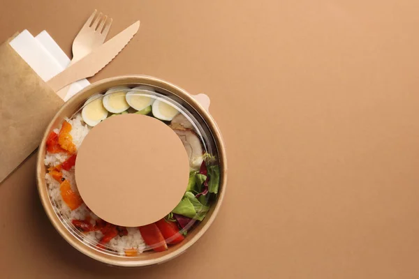 stock image Tasty food in container with wooden fork and knife on beige background, flat lay. Space for text