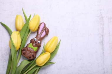 Çikolatalı Paskalya tavşanı ve beyaz desenli masa üzerinde güzel lalelerle bezenmiş düz bir kompozisyon. Metin için boşluk