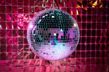 Shiny disco ball against foil party curtain under pink light clipart