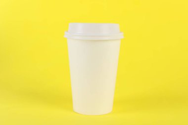 Sarı arka planda plastik kapaklı kağıt bardak. Kahve hazır.