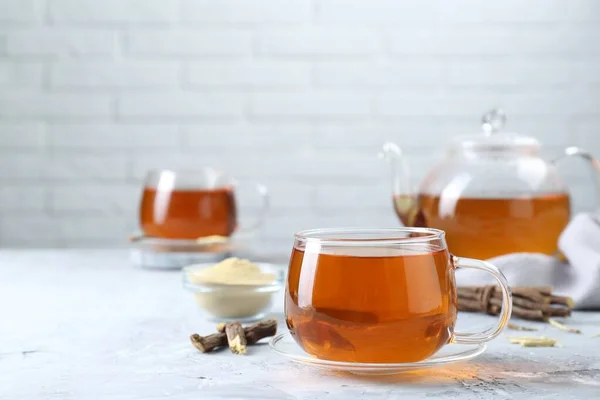 stock image Aromatic licorice tea and dried sticks of licorice root on light gray textured table, space for text