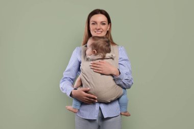 Anne zeytin arka planında çocuğunu askıda (bebek taşıyıcısı) tutuyor