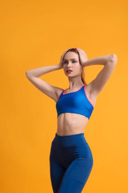 Sarı arka planda spor giyimli genç bir kadın.