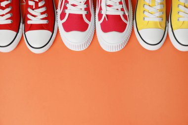 Turuncu arka planda, manzaranın üstünde farklı klasik eski moda spor ayakkabılar. Metin için boşluk