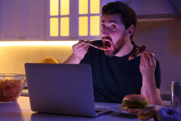 男人晚上在厨房用笔记本电脑吃披萨 坏习惯 — 图库照片